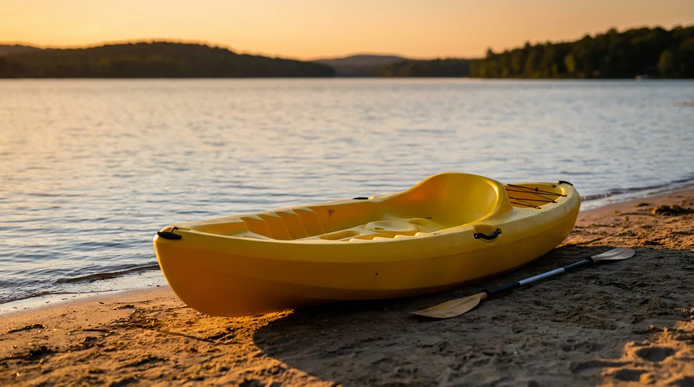 A stable sit-on-top kayak on a sandy lake shore during a golden sunset.