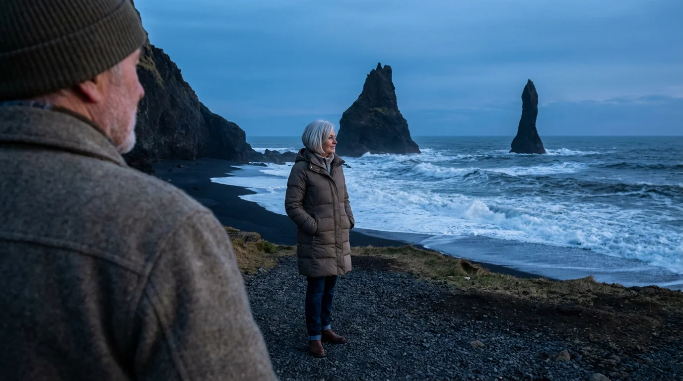 Senior couple watches the sunset over the basalt columns of Reynisfjara black sand beach.